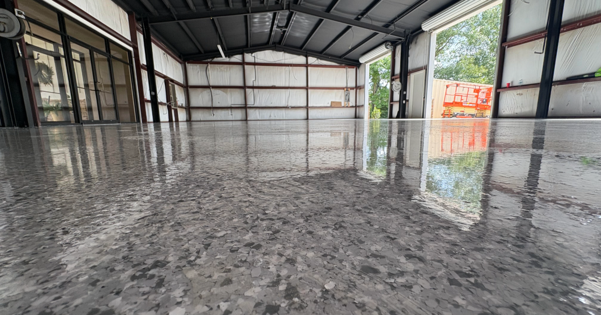 Empty industrial warehouse with a shiny wet concrete floor and exposed metal beams interior.